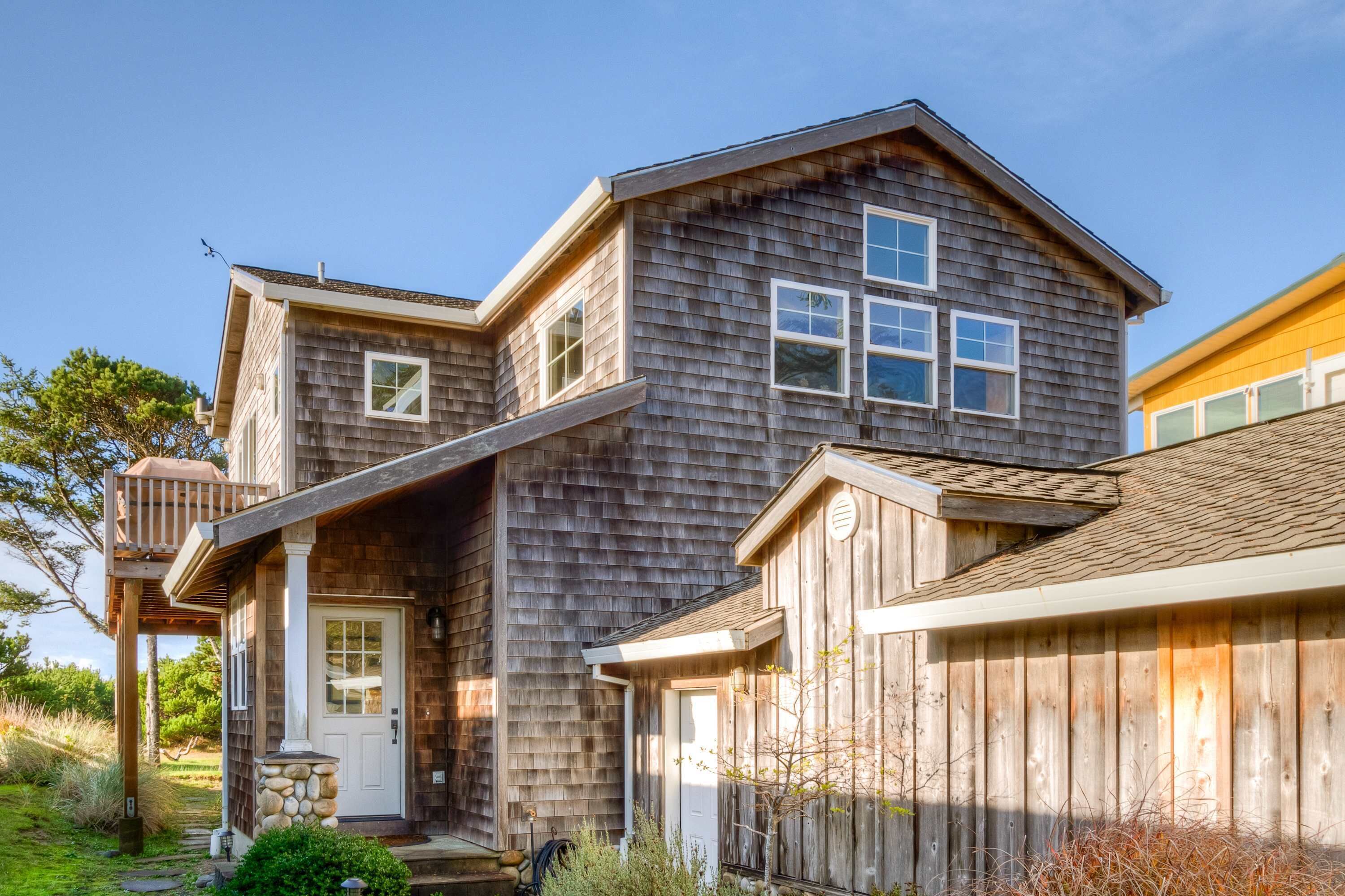 A two-story wooden house with a front porch, a stone foundation, and a small garden area.