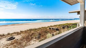 Vista de una playa desde un balcón, con arena, olas del océano y cielo despejado.