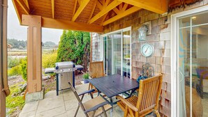Une terrasse extérieure avec une table et des chaises en bois, un barbecue et un thermomètre.