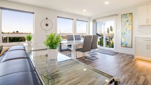 Una sala de estar moderna con una mesa de comedor de vidrio, asientos cómodos y grandes ventanales con vistas.