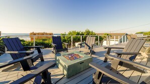 Una terraza con sillas Adirondack, una mesa de vidrio y vistas al océano.