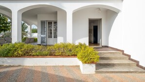 Ein weißes Gebäude mit drei Bögen, einer Treppe und einem kleinen Garten.