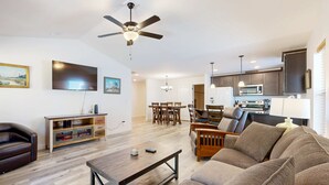 A modern living room with a sofa, coffee table, TV, and ceiling fan. - Indulge in Ocean Bliss Where Elegance Meets Ocean Breeze (Rockaway Beach)