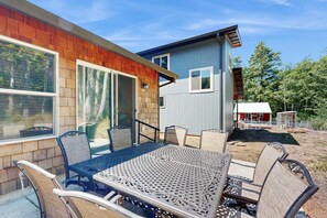 Une terrasse extérieure avec une table et des chaises en métal, une terrasse en bois et une maison à l’extérieur bleue avec un garage rouge.