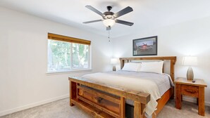 A bedroom with a wooden bed, a ceiling fan, a window, a bedside table with a lamp, and a framed picture on the wall. - Indulge in Ocean Bliss Where Elegance Meets Ocean Breeze (Rockaway Beach)
