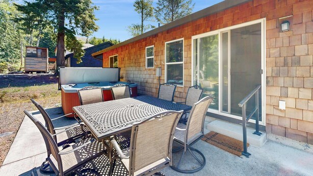An outdoor patio area with a metal table and chairs, a hot tub, and a wooden deck. - Indulge in Ocean Bliss Where Elegance Meets Ocean Breeze (Rockaway Beach)