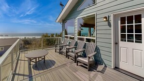 Um terraço com cadeiras Adirondack e uma mesa, com vista para um cenário oceânico.