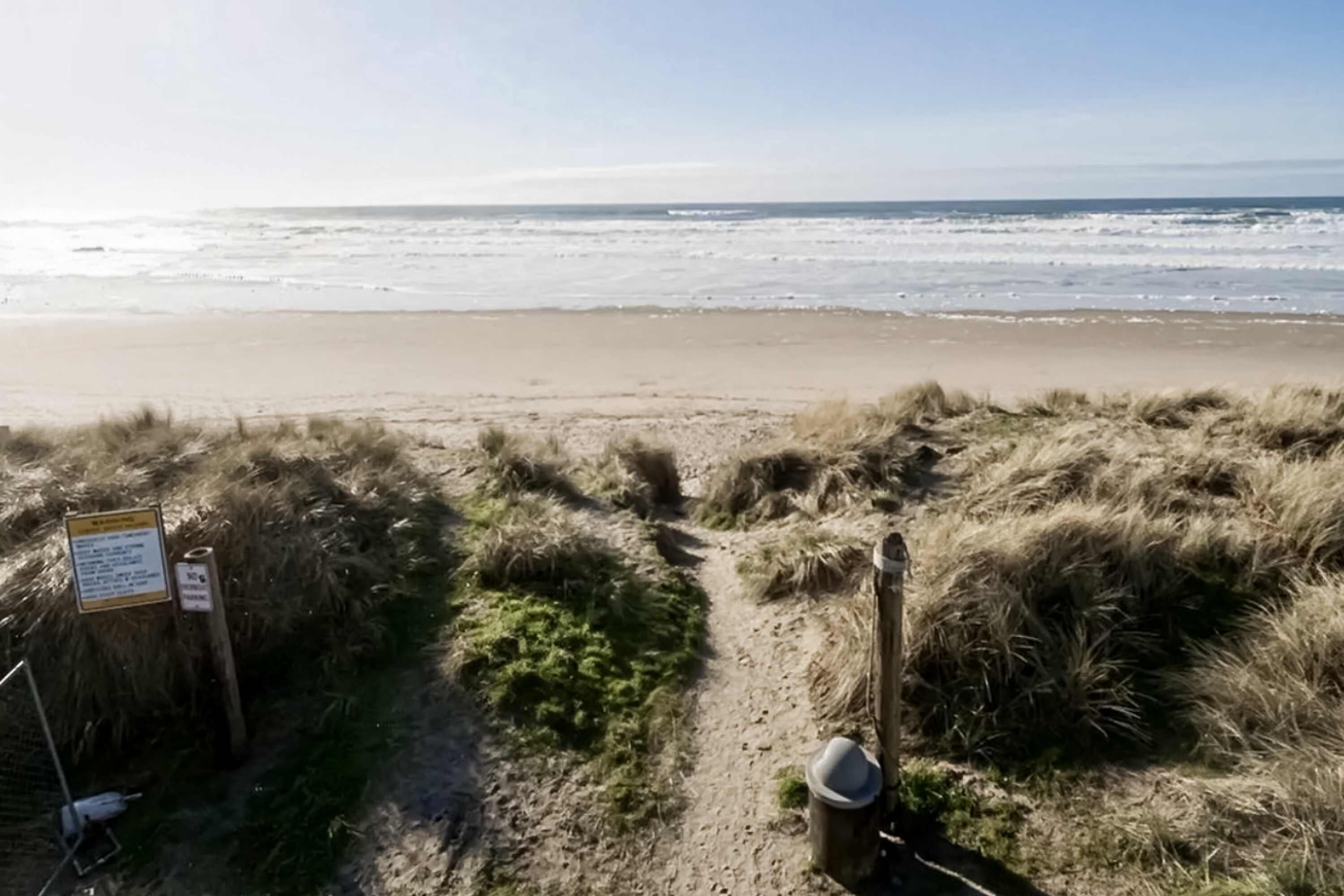 Een strandpad dat naar de oceaan leidt, met een bord en een metalen bak.