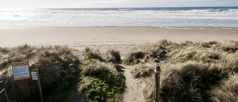 Een strandpad dat naar de oceaan leidt, met een bord en een metalen bak.