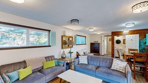 Ein Wohnzimmer mit zwei Sofas, einem Couchtisch und einem Fernseher. Es gibt einen Essbereich mit Tisch und Stühlen.