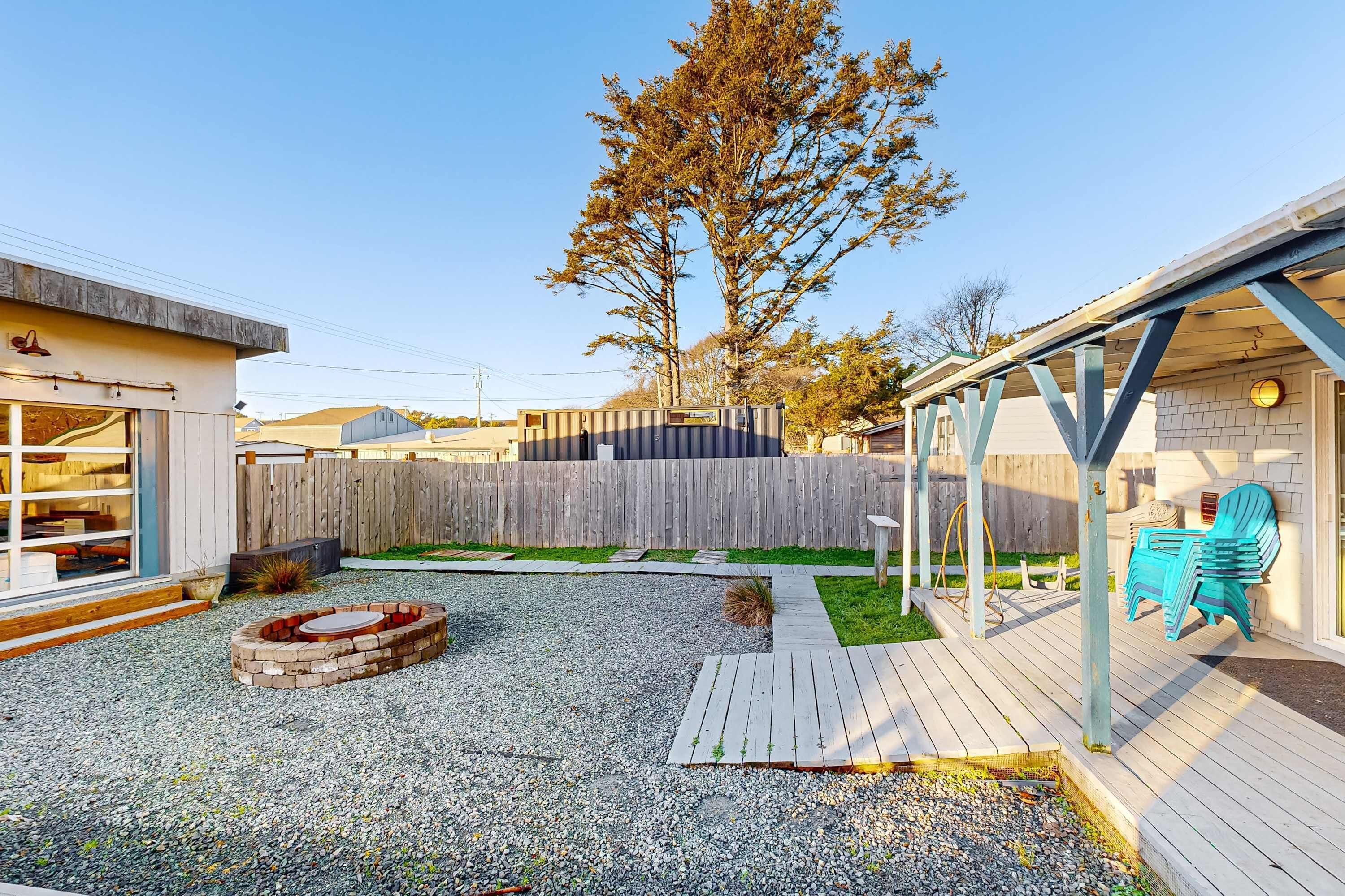 A backyard with a wooden deck, a fire pit, and a fenced area.