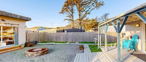 A backyard with a wooden deck, a fire pit, and a fenced area.