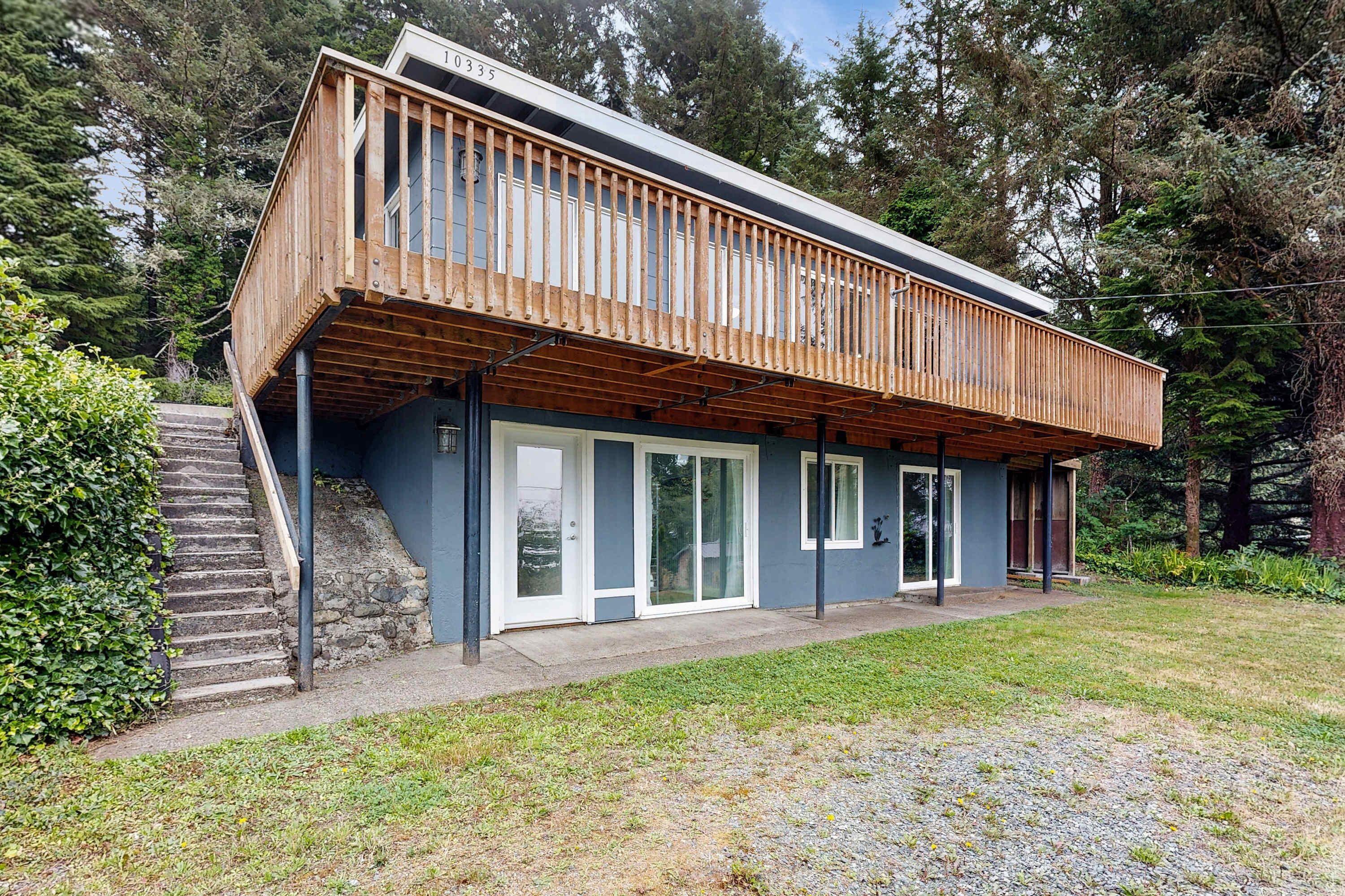 A modern house with a wooden deck, large sliding glass doors, and a stone staircase leading to a door.
