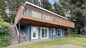A modern house with a wooden deck, large sliding glass doors, and a stone staircase leading to a door. - Spacious dog friendly home with ocean views full kitchen washer and dryer (Rockaway Beach)