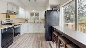 A modern kitchen with white cabinets, stainless steel appliances, and a large window offering a view of the outdoors. - Spacious dog friendly home with ocean views full kitchen washer and dryer (Rockaway Beach)