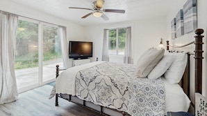 A bedroom with a bed, a ceiling fan, a TV, and large windows. - Spacious dog friendly home with ocean views full kitchen washer and dryer (Rockaway Beach)