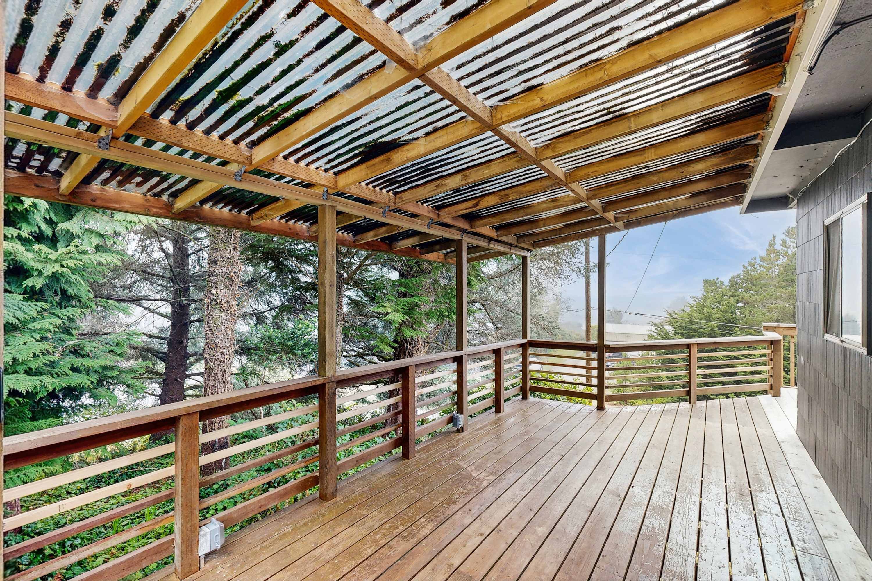 Una terraza de madera con estructura de techo metálico, rodeada de árboles.
