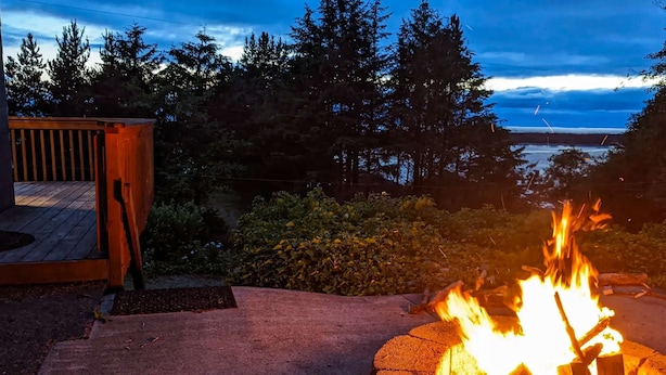 A fire pit with logs, a wooden deck, and a view of trees and a body of water. - Spacious dog friendly home with ocean views full kitchen washer and dryer (Rockaway Beach)
