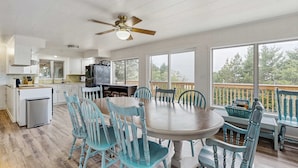 A spacious kitchen with white cabinets, a dining area with a large table and blue chairs, and a balcony with a view of trees. - Spacious dog friendly home with ocean views full kitchen washer and dryer (Rockaway Beach)
