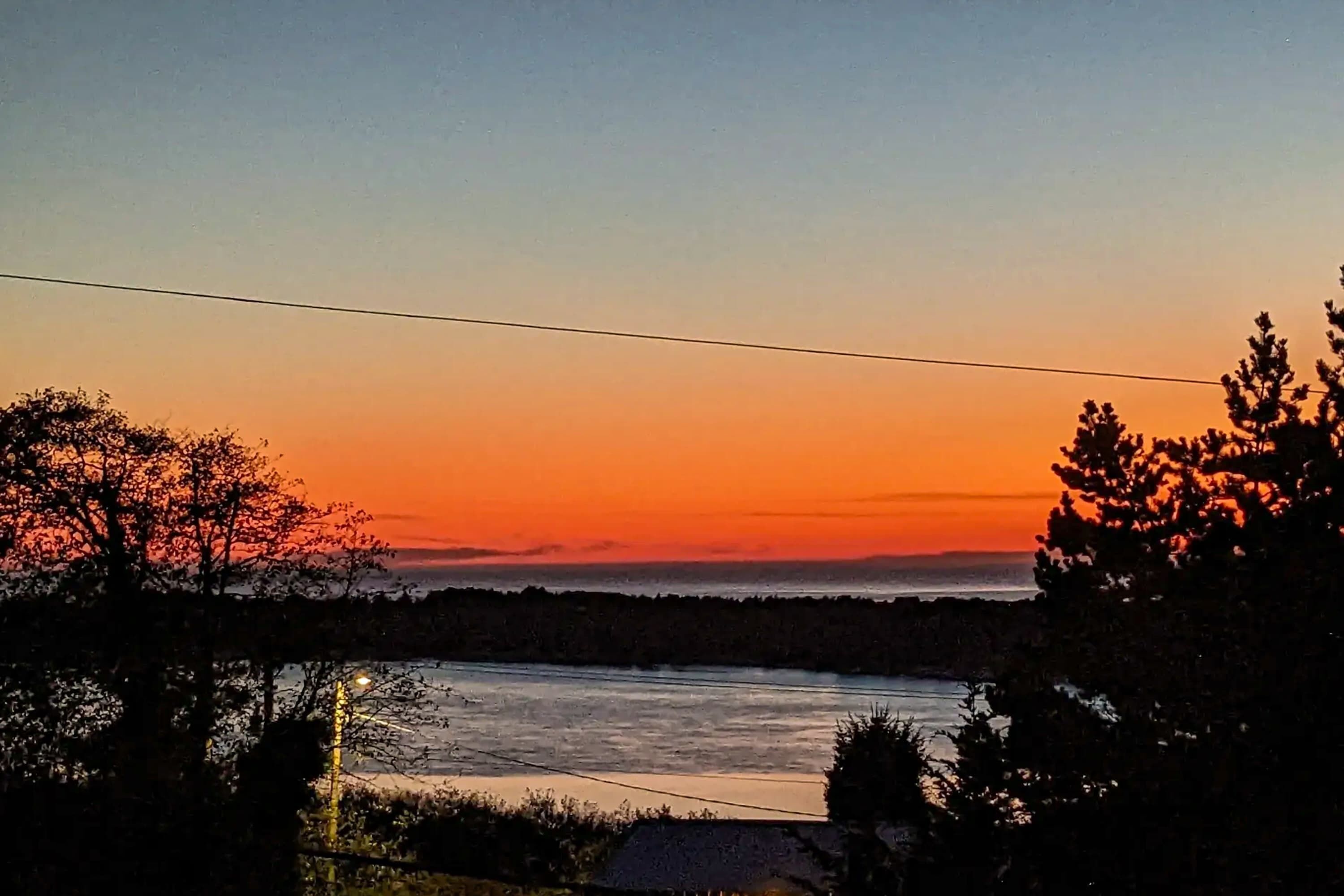 A sunset over a body of water with trees silhouetted against the sky.
