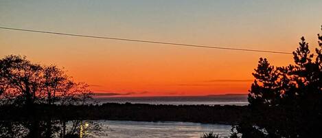 A sunset over a body of water with trees silhouetted against the sky.