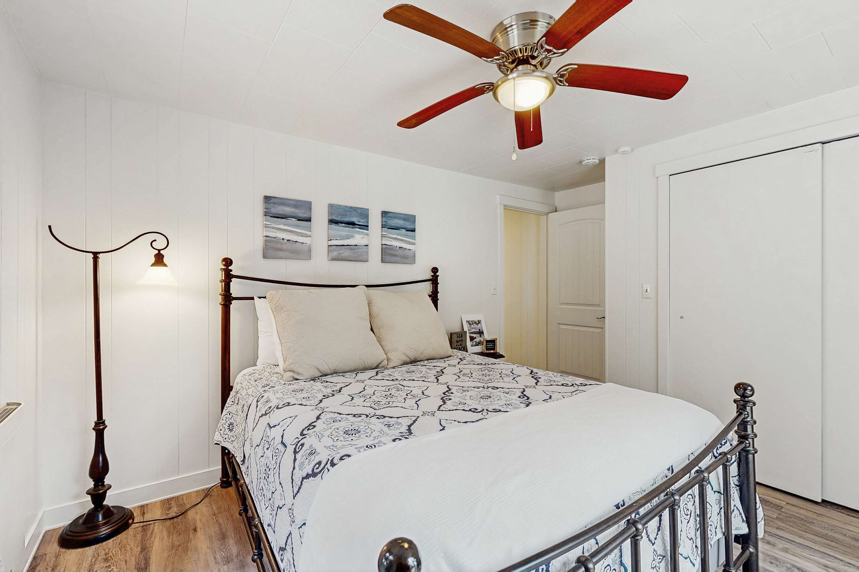 A bedroom with a bed, a ceiling fan, a floor lamp, and a door.