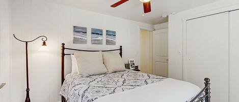 A bedroom with a bed, a ceiling fan, a floor lamp, and a door.