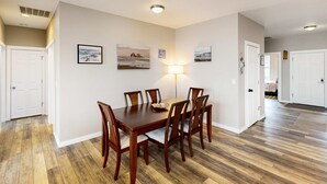 A dining area with a wooden table and chairs, a wall-mounted lamp, and framed pictures. - Spacious retreat with beautiful ocean views dog friendly with WiFi patio (Rockaway Beach)