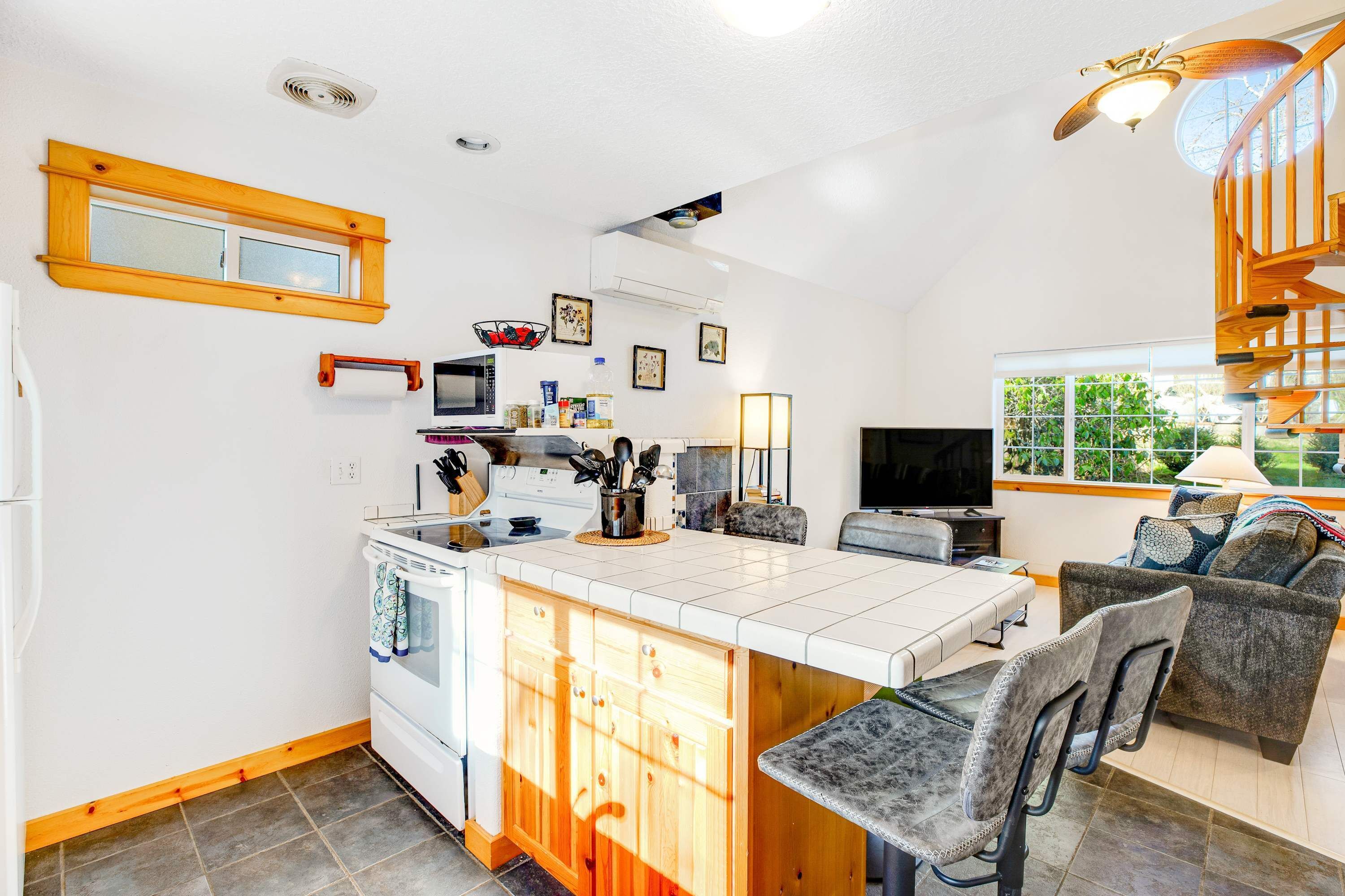 A compact kitchen with a central island, a dining area with a sofa, and a staircase leading to an upper level.