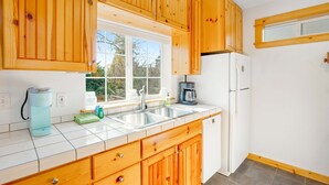 A kitchen with wooden cabinets, a white refrigerator, a coffee maker, and a window. - Two story getaway with a washer dryer central AC and WiFi dogs welcome (Tillamook)