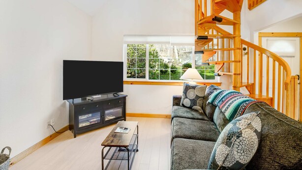 A living room with a flat-screen TV, a sofa, a coffee table, and a wooden staircase. - Two story getaway with a washer dryer central AC and WiFi dogs welcome (Tillamook)