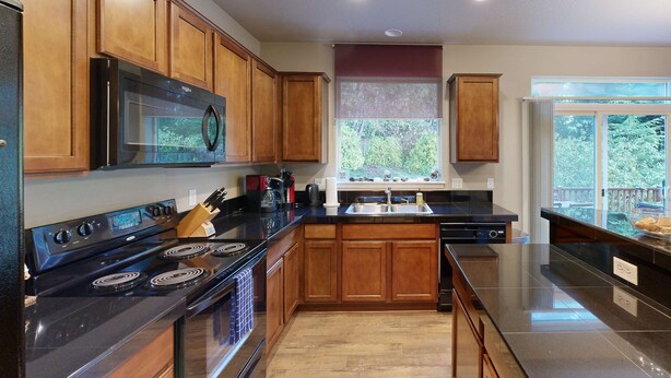 A modern kitchen with wooden cabinets, a black stove, and a large window with a view of greenery. - Modern Ocean Highlands home with Netarts Bay and ocean views fireplace dogs OK (Tillamook)