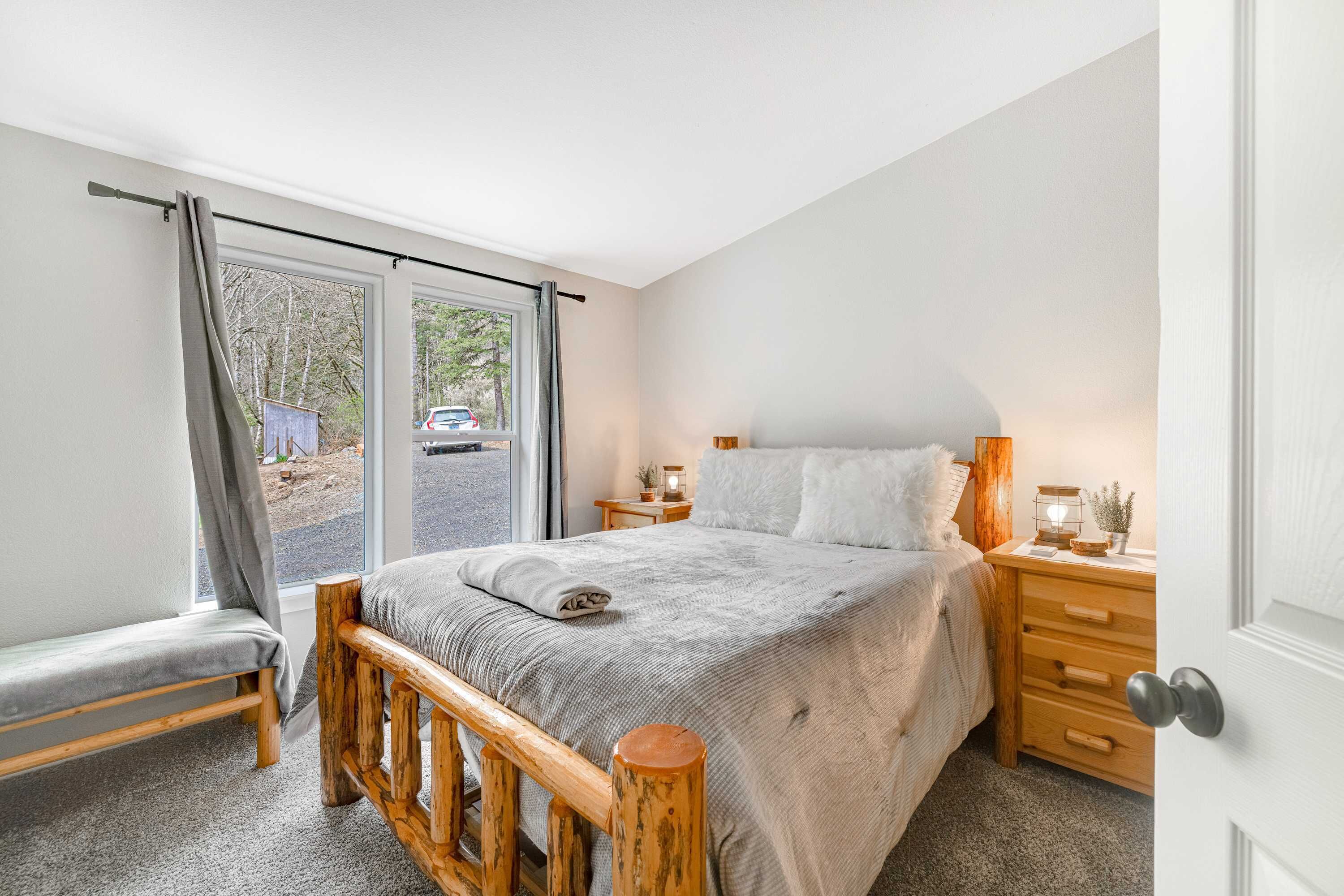 A bedroom with a large bed, wooden headboard, a bench, and a nightstand with a lamp.
