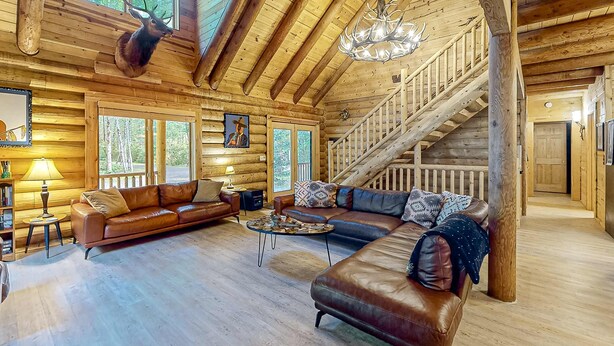 L’intérieur d’une cabane en rondins, avec un grand escalier en bois, des canapés en cuir et une tête de cerf accrochée au mur.