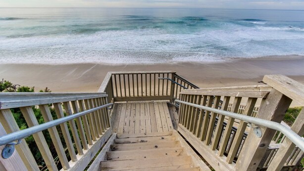 Un escalier en bois menant à une plage d’où l’on a une vue sur l’océan.