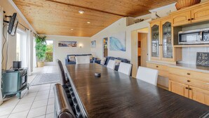 A spacious kitchen with wooden cabinets, a large dining table, and a view to a balcony. - Ocean View Home with Rec Room Rock Wall and Private Hot Tub A Block From Beach (Rockaway Beach)