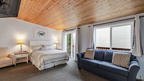 A bedroom with a bed, a sofa, a nightstand, a lamp, and a window with curtains. - Ocean View Home with Rec Room Rock Wall and Private Hot Tub A Block From Beach (Rockaway Beach)