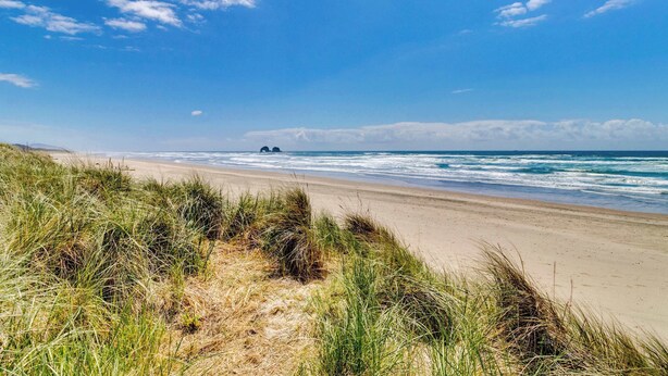 A beach with sand dunes and ocean waves. - Ocean View Home with Rec Room Rock Wall and Private Hot Tub A Block From Beach (Rockaway Beach)