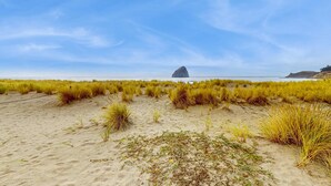 Une plage de sable, avec de l’herbe et, au loin, une formation rocheuse.