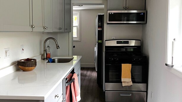 A modern kitchen with white cabinets, stainless steel appliances, and a wooden floor.