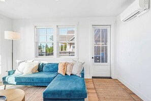 Un salon moderne avec un canapé d’angle bleu, une lampe sur pied et une vue par les fenêtres.