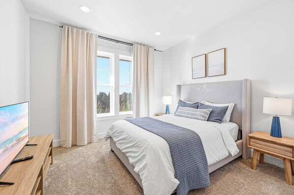 A modern hotel room with a large bed, a TV, and a window with curtains.