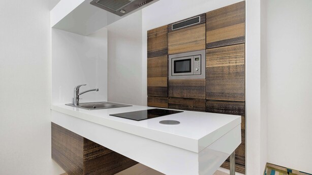 Una cocina moderna con encimera blanca, pileta de acero inoxidable y microondas.