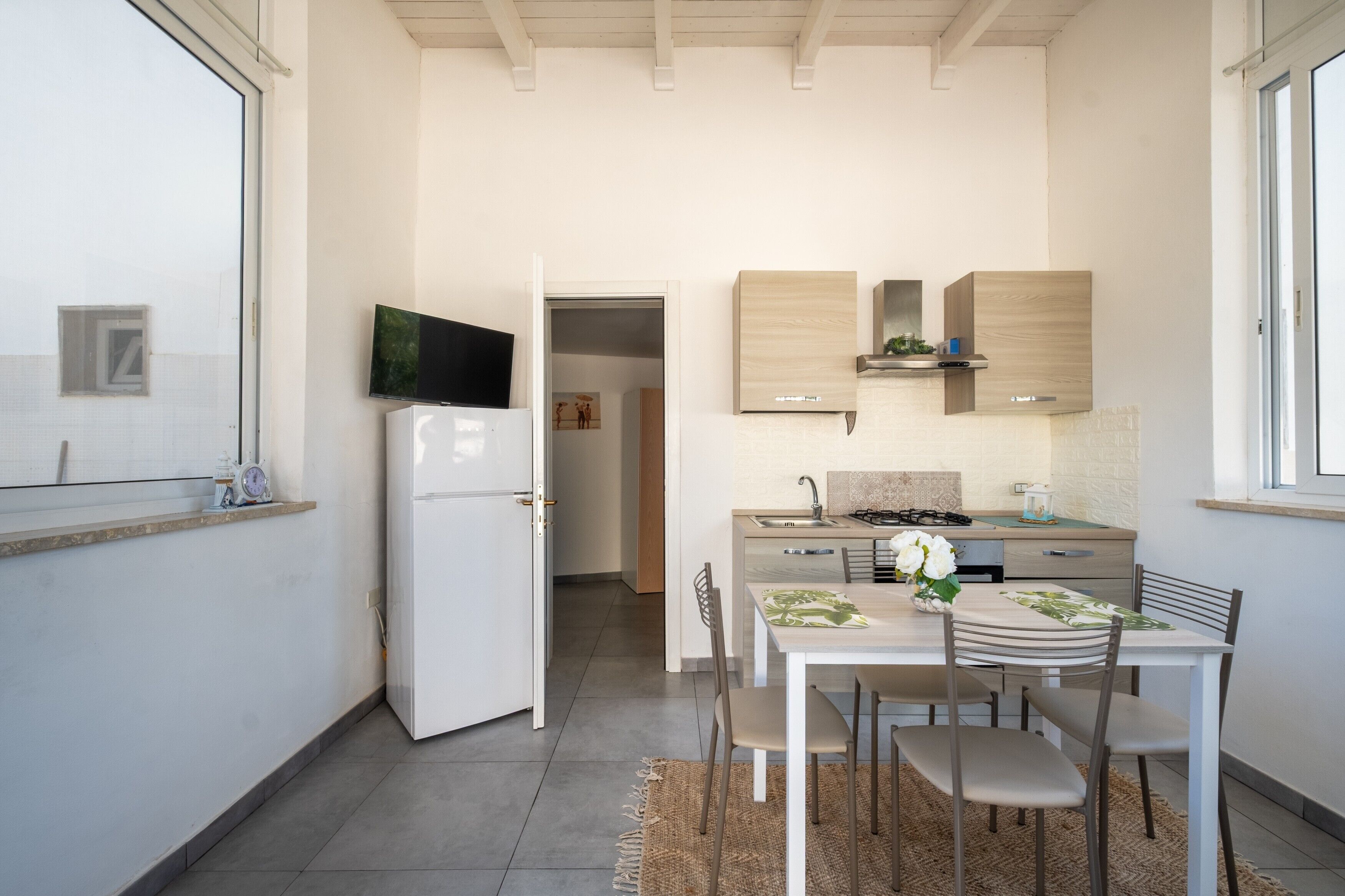 Eine moderne Küche mit Kühlschrank, Herd und Schränken. Ein Esstisch mit Stühlen und einem Teppich sind ebenfalls vorhanden.