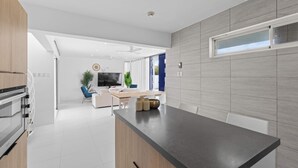 A modern kitchen with a central island, built-in appliances, and a dining area with a TV and seating. - Villa Santorini – Luxury 4-Bedroom Villa with Pool, Gym & Outdoor Living in Brakkeput, Curaçao (Willemstad)