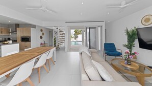 A modern living space with a wooden dining table, white chairs, a beige sofa, a blue armchair, and a TV on the wall. - Villa Santorini – Luxury 4-Bedroom Villa with Pool, Gym & Outdoor Living in Brakkeput, Curaçao (Willemstad)