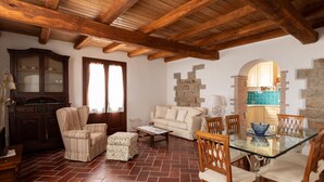 A living room with a glass-top dining table, wooden chairs, a sofa, a striped armchair, a cabinet, and a stone wall. - Casa al Duomo by Wonderful Italy (Telti)
