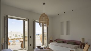 A modern living room with a large window, a round coffee table, a sofa, and a chair. - Casa Botanica · Heather (Antiparos)