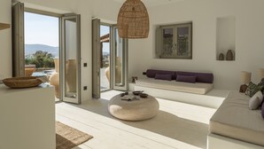 Ein modernes Wohnzimmer mit großem Fenster, rundem Ottoman, einer Couch mit Kissen und einer Pendelleuchte.