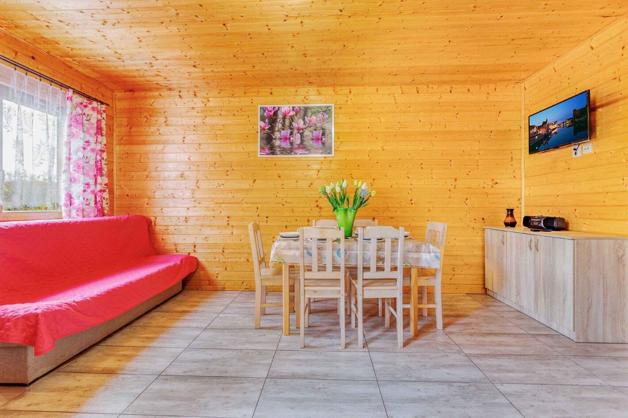 A wooden interior with a red sofa, a dining table with chairs, a cabinet, and a painting on the wall.